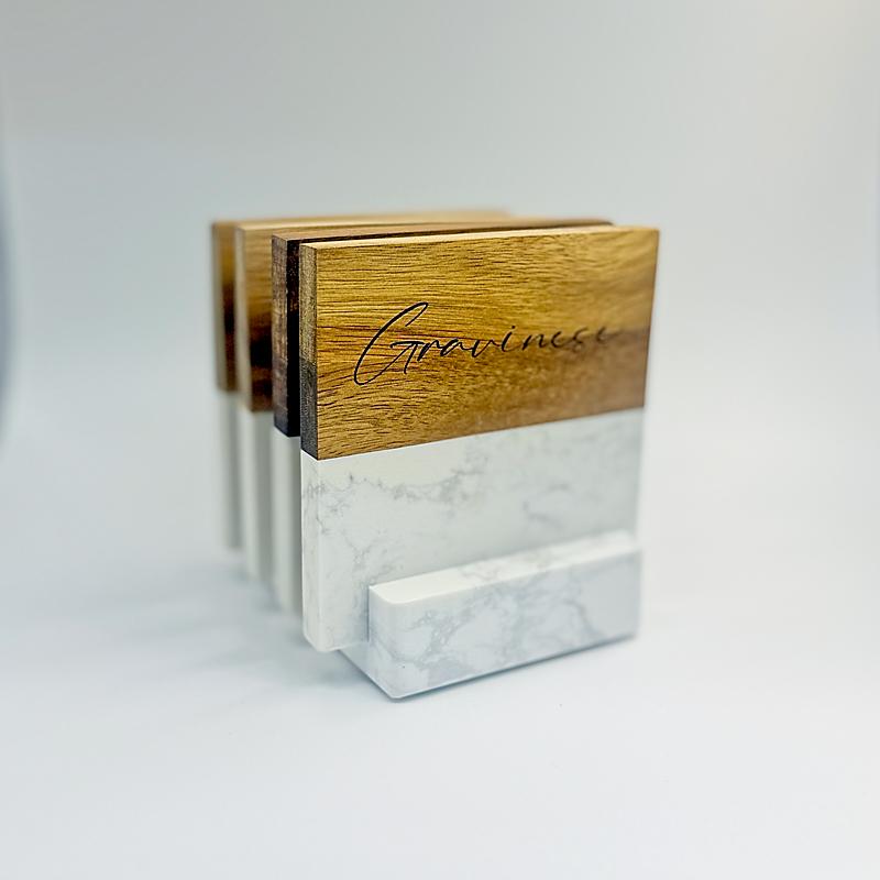Four personalized marble-and-acacia-wood coasters displayed in a heavy marble stand.